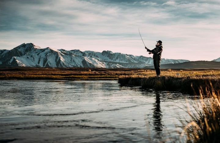 Fishing - landscape photo of man fishing on river near mountain alps