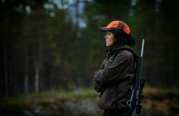 Hunter - woman carrying hunting rifle in woods